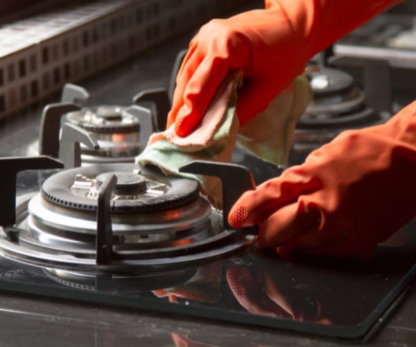 gloved hands cleaning natural gas cooktop
